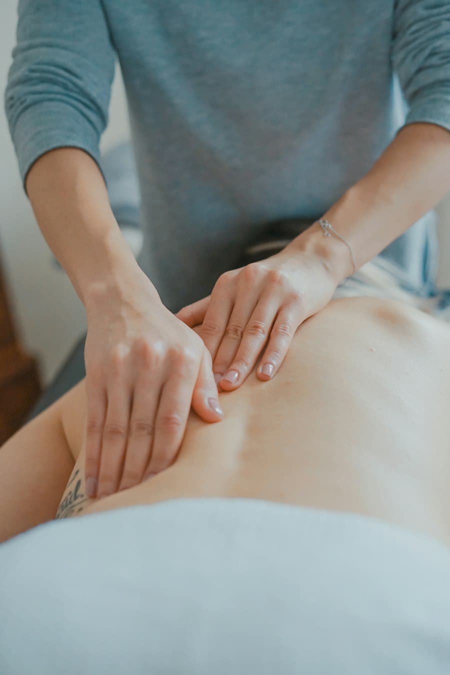 Mãos de fisioterapeuta realizando terapia manual nas costas de uma paciente